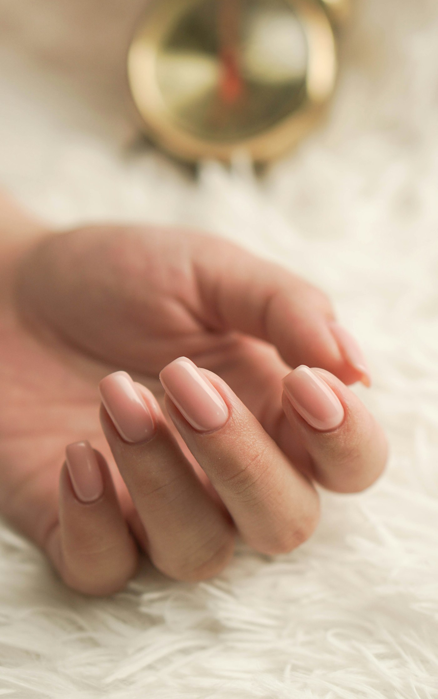 Leona Nails – Nude Maniküre Gepflegte Hand mit zartrosa Maniküre auf weichem weissem Fell