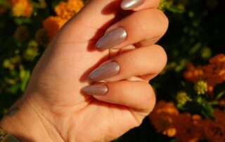 Galerie – Maniküre mit Blumen Manikürte Hand hält Blumen vor orangefarbenen Blüten